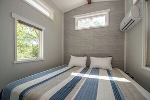 Ein Schlafzimmer mit einem Bett, zwei Fenstern und einer Klimaanlage.