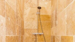 A shower with a handheld showerhead and a wall-mounted control valve, set in a tiled room with a white floor.