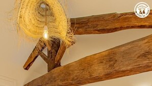 A bedroom with a wooden ceiling beam, a bed with white bedding, and a hanging light fixture.