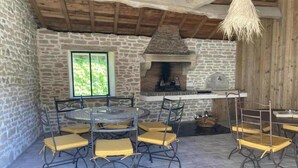 A stone-walled room with a fireplace, a round table with chairs, and a hanging light fixture.