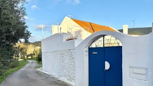 A white building with a blue gate, a clear sky, and a road leading to it. - Servigueira by Grota Lodging (Leiria)