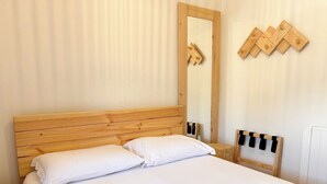 A bed with white bedding, a wooden headboard, a large mirror, and a wooden nightstand with a black object on it. - Servigueira by Grota Lodging (Leiria)