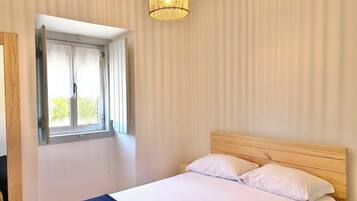 A bedroom with a bed, a window with curtains, a wooden headboard, and a hanging light fixture.