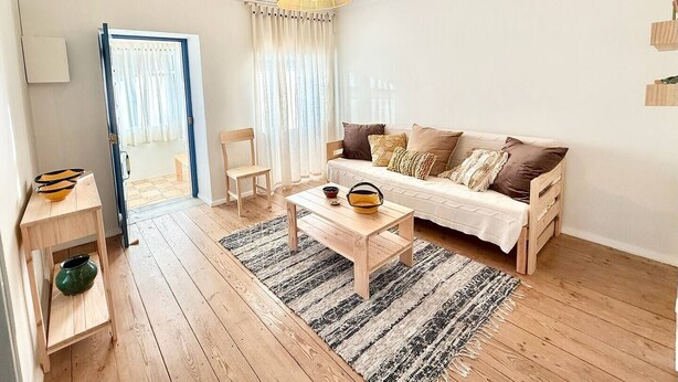 A living room with a sofa, a coffee table, a chair, a hanging light fixture, and a door leading to another room. - Servigueira by Grota Lodging (Leiria)