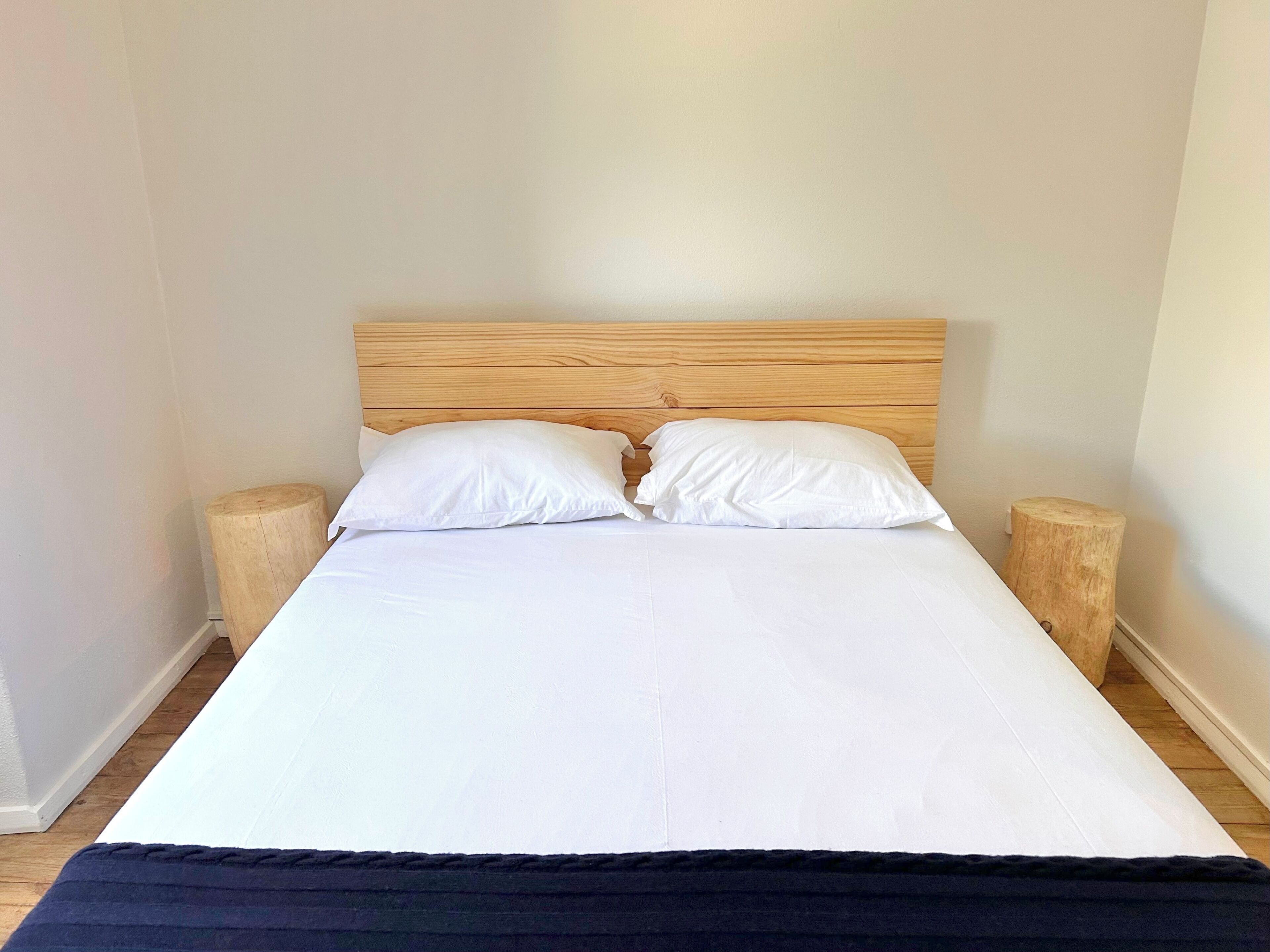 Un letto con testiera in legno, due cuscini bianchi e due comodini in legno.