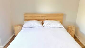 Un letto con testiera in legno, due cuscini bianchi e due comodini in legno.