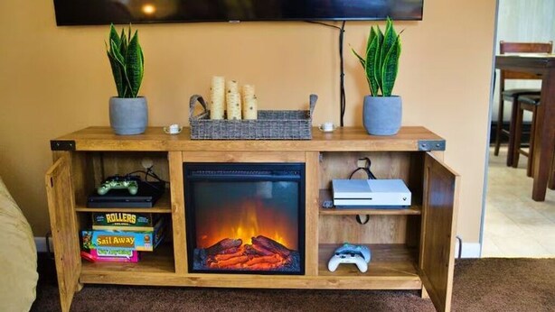 Un meuble de rangement en bois pour les appareils multimédias, doté d’une cheminée, de consoles de jeux et de jeux de société.