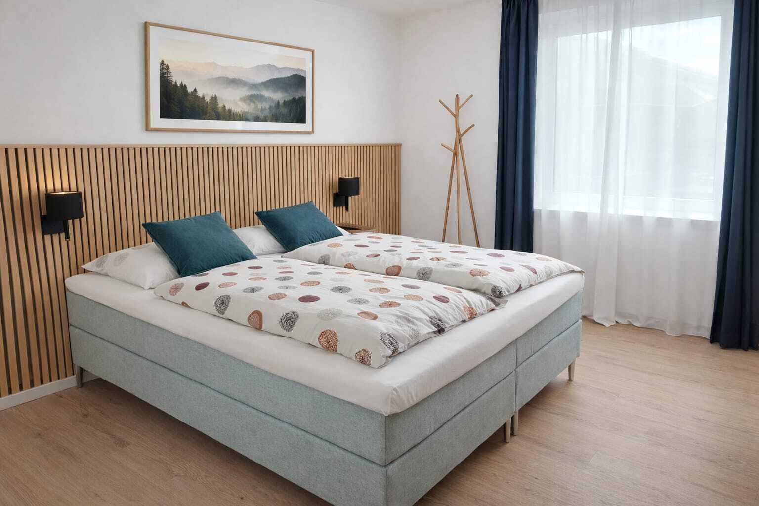 Un lit double avec une couette à motifs, une tête de lit en bois, un tableau accroché au mur et une lampe sur pied.