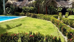 Ein Resort mit strohgedeckten Gebäuden, einem Schwimmbad und üppiger tropischer Bepflanzung.