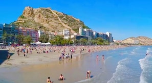 A beach with a large hill, buildings, and people. - La Reina Apartment by the Sea (Alicante (Alacant))