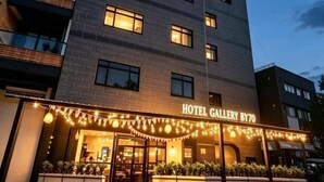 Un hotel amb un cartell que diu 'HOTEL GALLERY BY70', diverses plantes i una lluna creixent al cel.