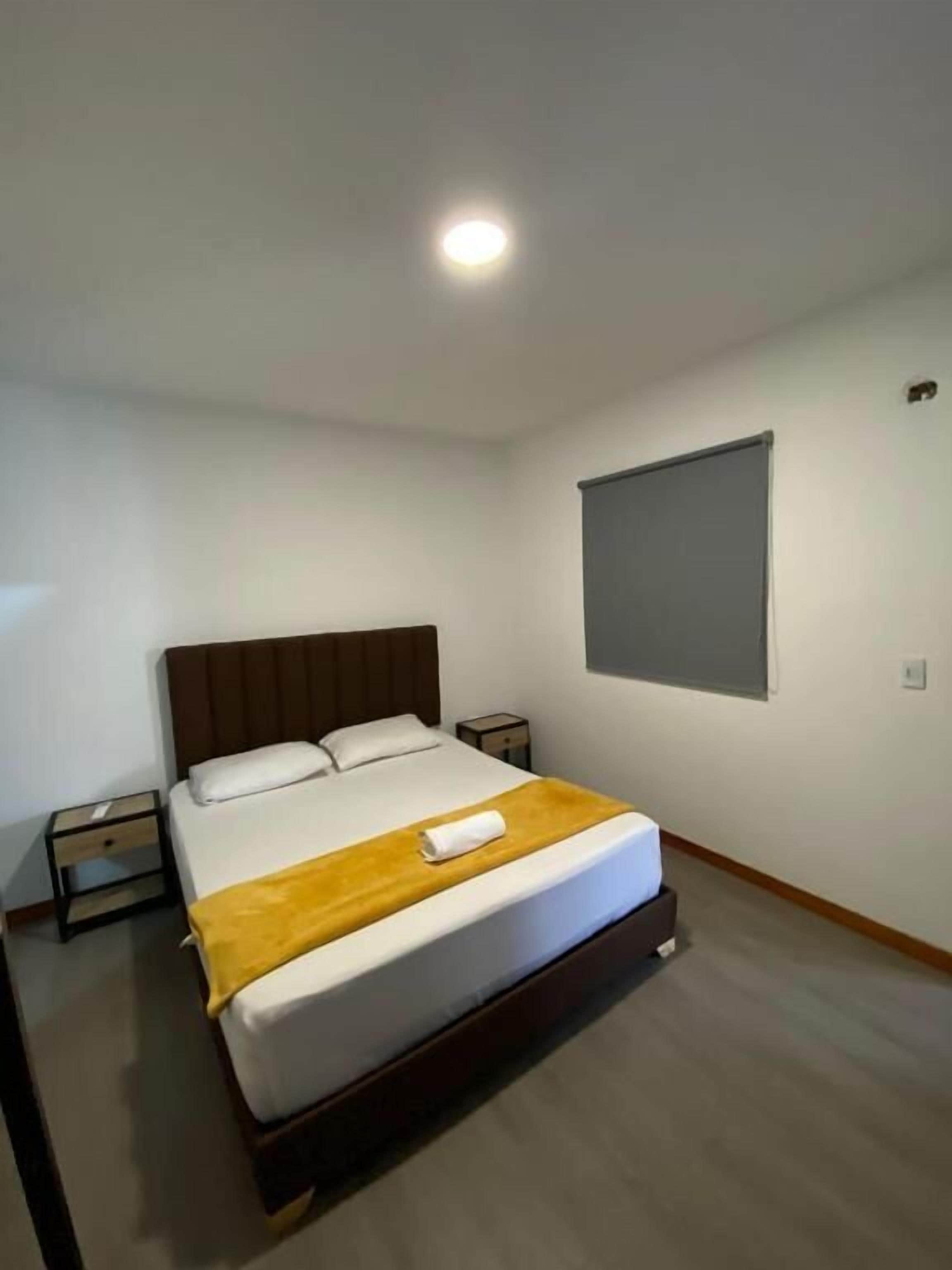 A hotel room with a bed, bedside tables, a window, and a ceiling light.