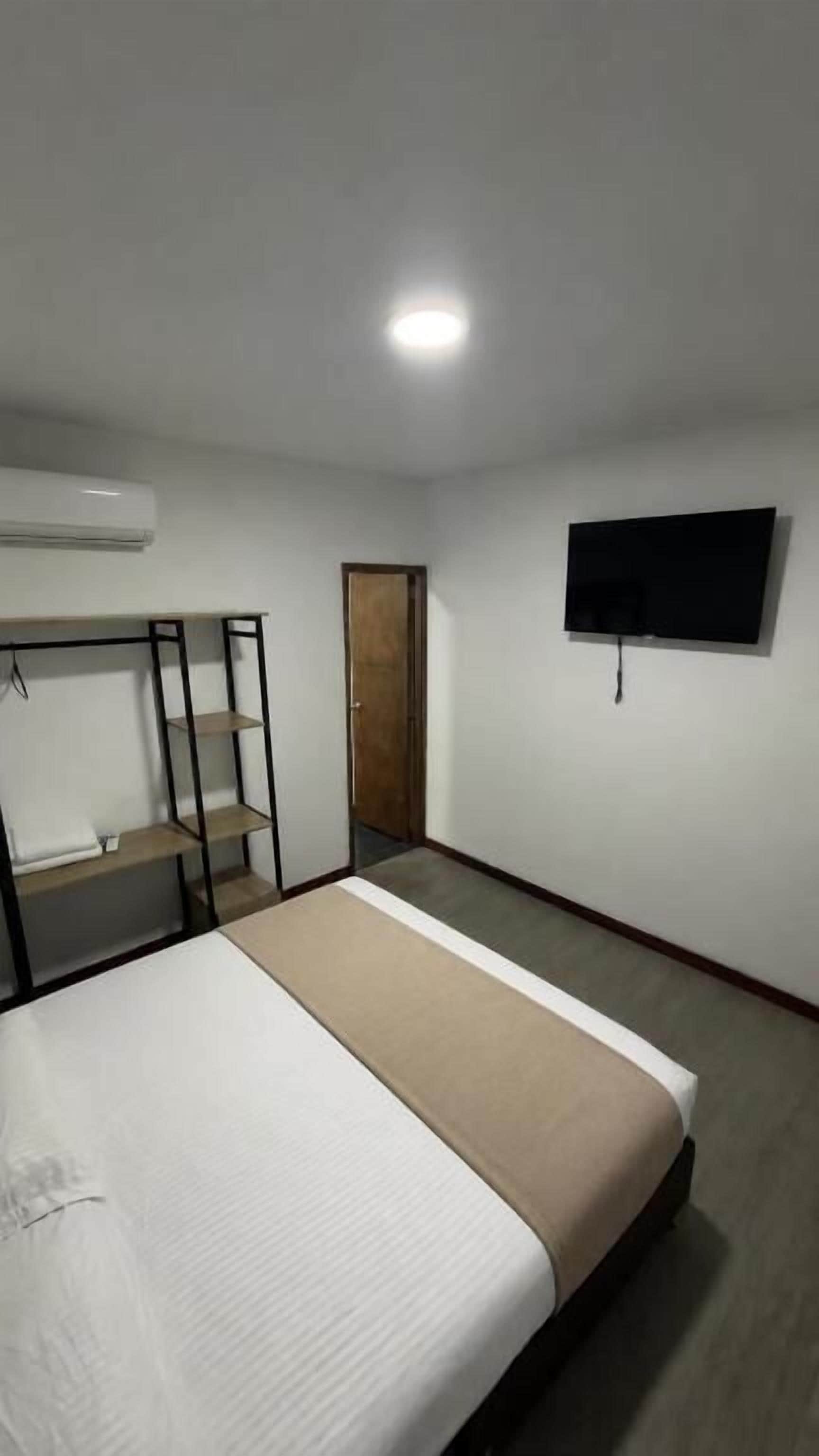 Una habitación con una cama, televisor en la pared, armario y una puerta.