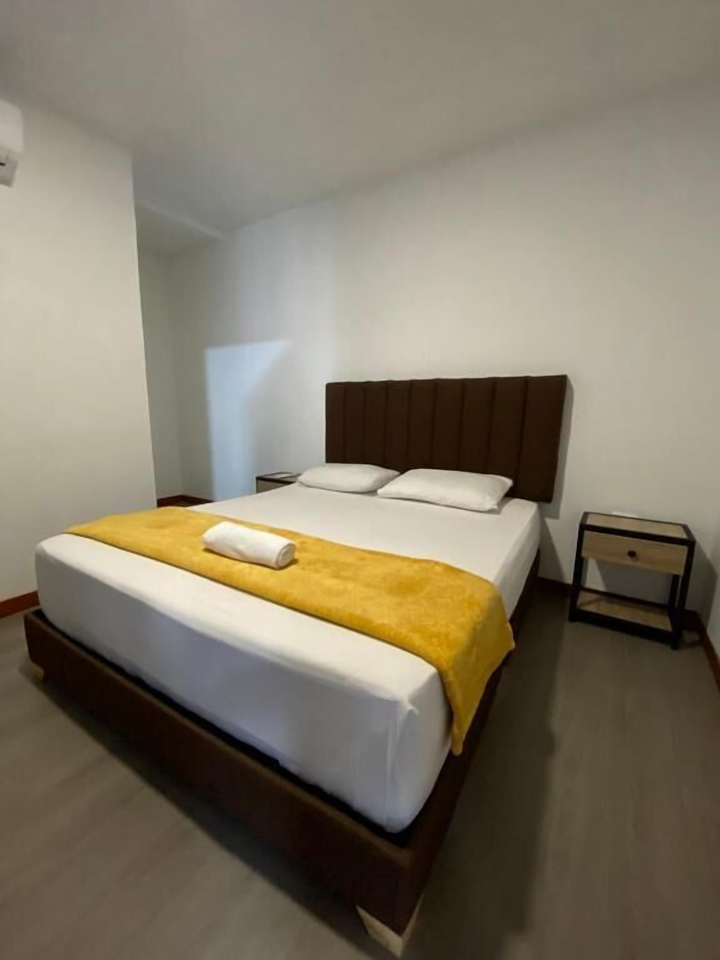 Una cama individual con cabecera de madera, una manta amarilla y una almohada blanca.