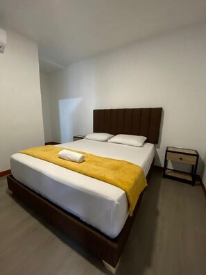 Un lit simple avec une tête de lit en bois, une couverture jaune et un oreiller blanc.
