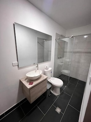 A modern bathroom with a white sink, toilet, and glass shower enclosure. - Hotel Gallery By 70 (Medellín)
