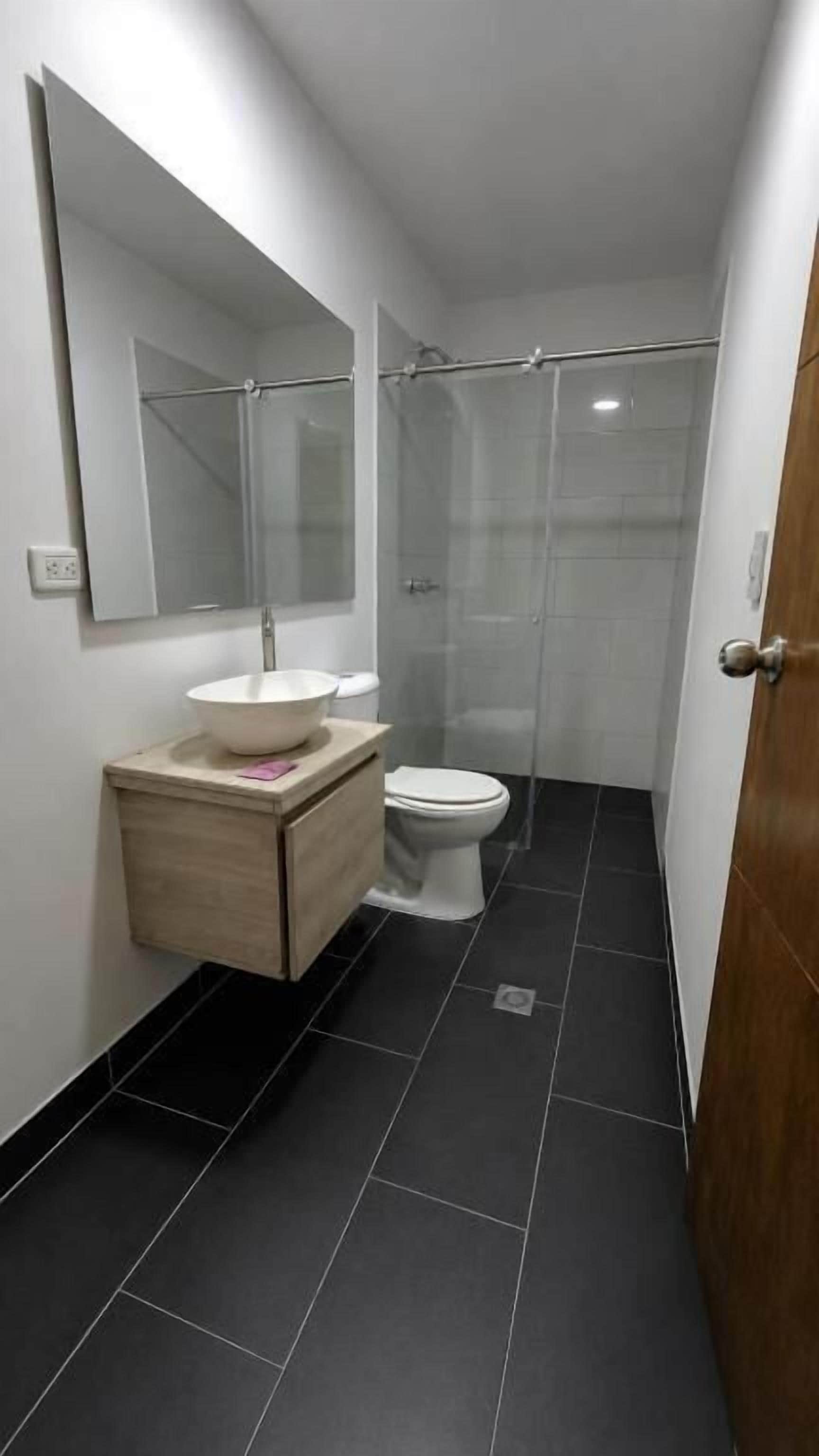 Un baño con inodoro, lavamanos con espejo y cabina de ducha con mampara de vidrio.