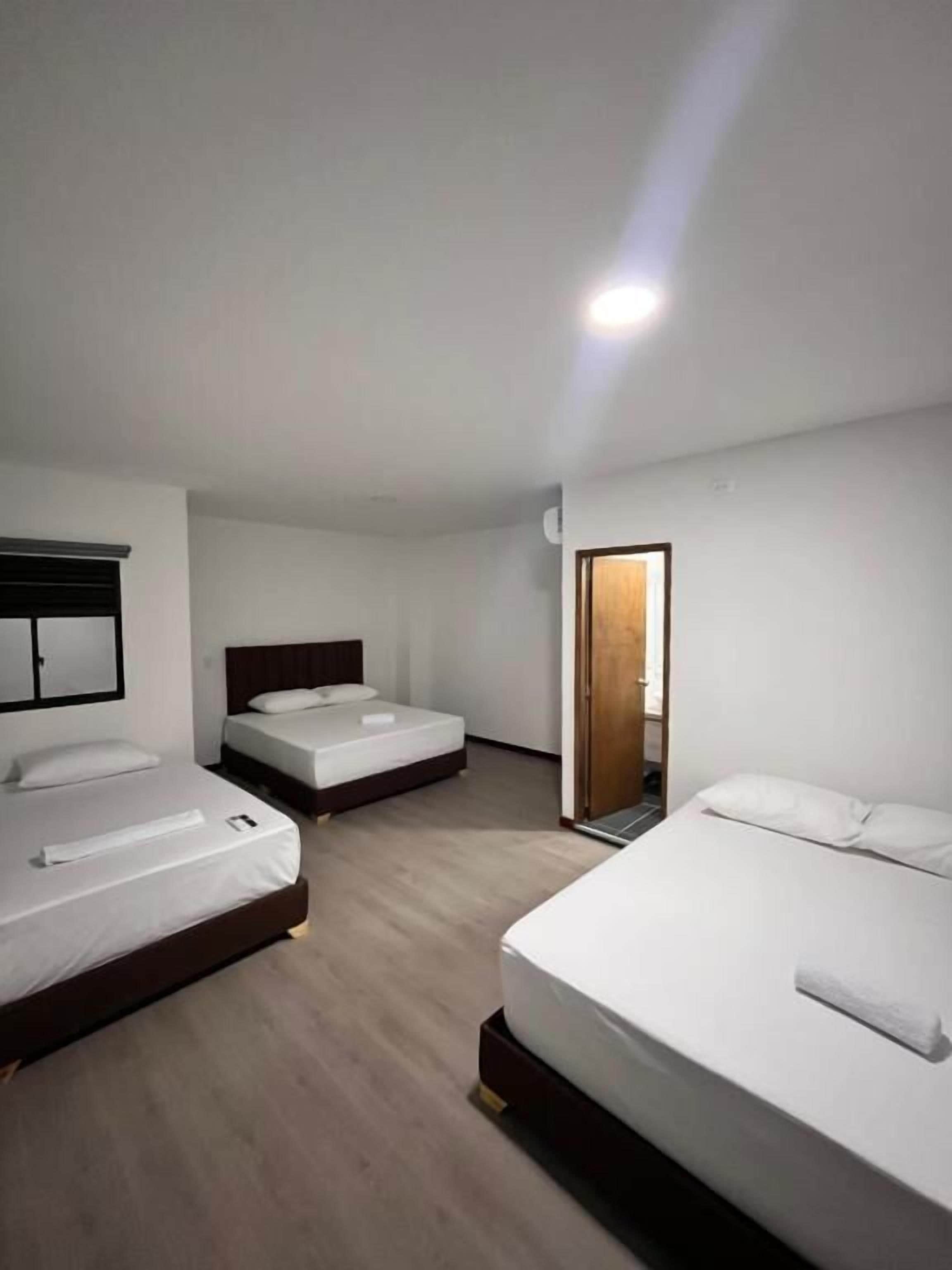 A hotel room with three beds, a wooden floor, and a door leading to another room.