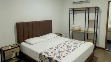 A bedroom with a bed, a nightstand, a wardrobe, and an air conditioning unit.