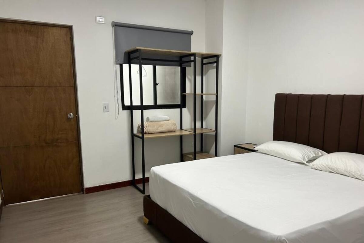 A bedroom with a bed, a wardrobe, a shelf unit, and a bedside table.