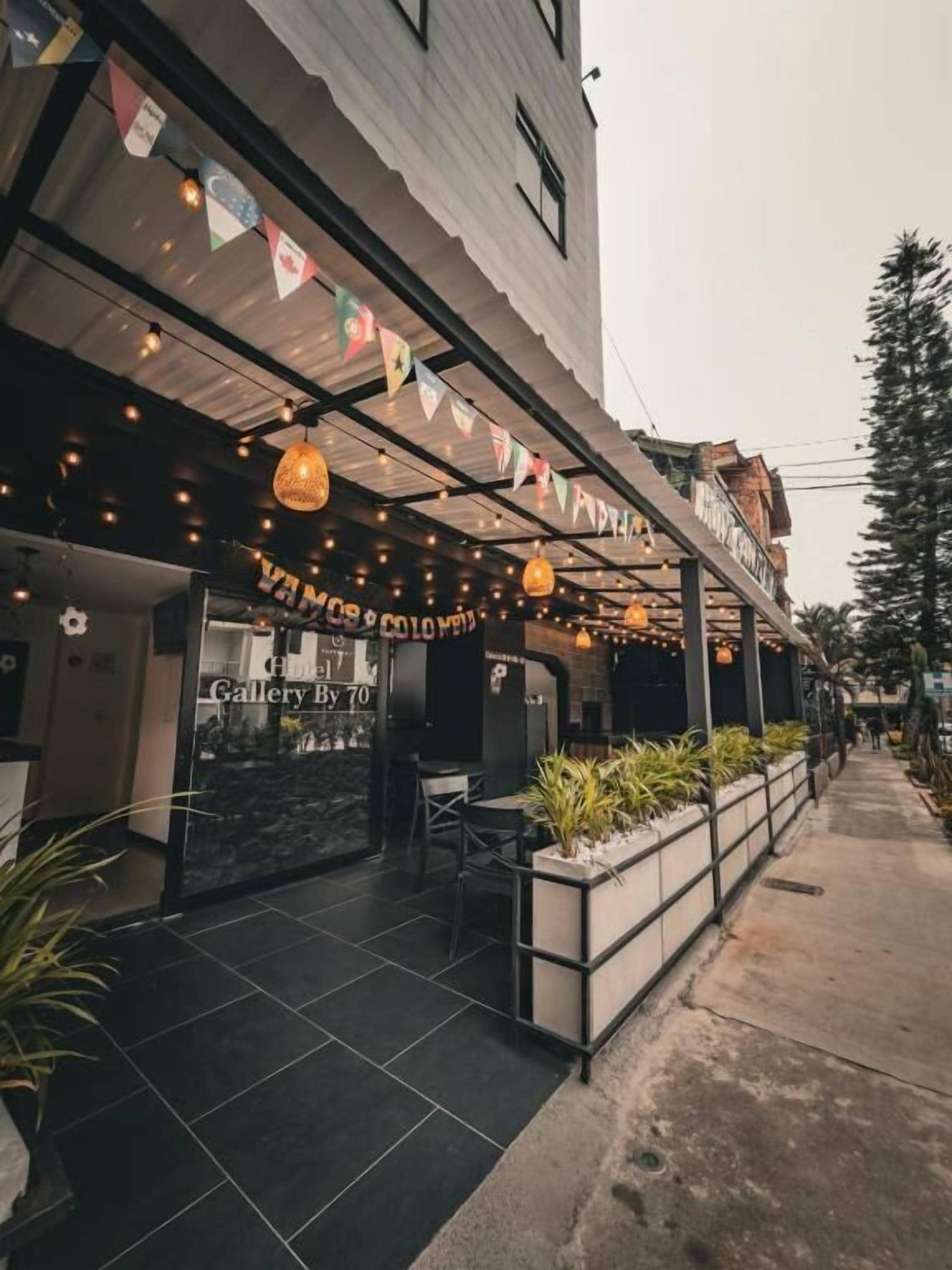 Exterior de hotel com área de estar coberta ao ar livre, entrada visível e uma placa indicando uma galeria.
