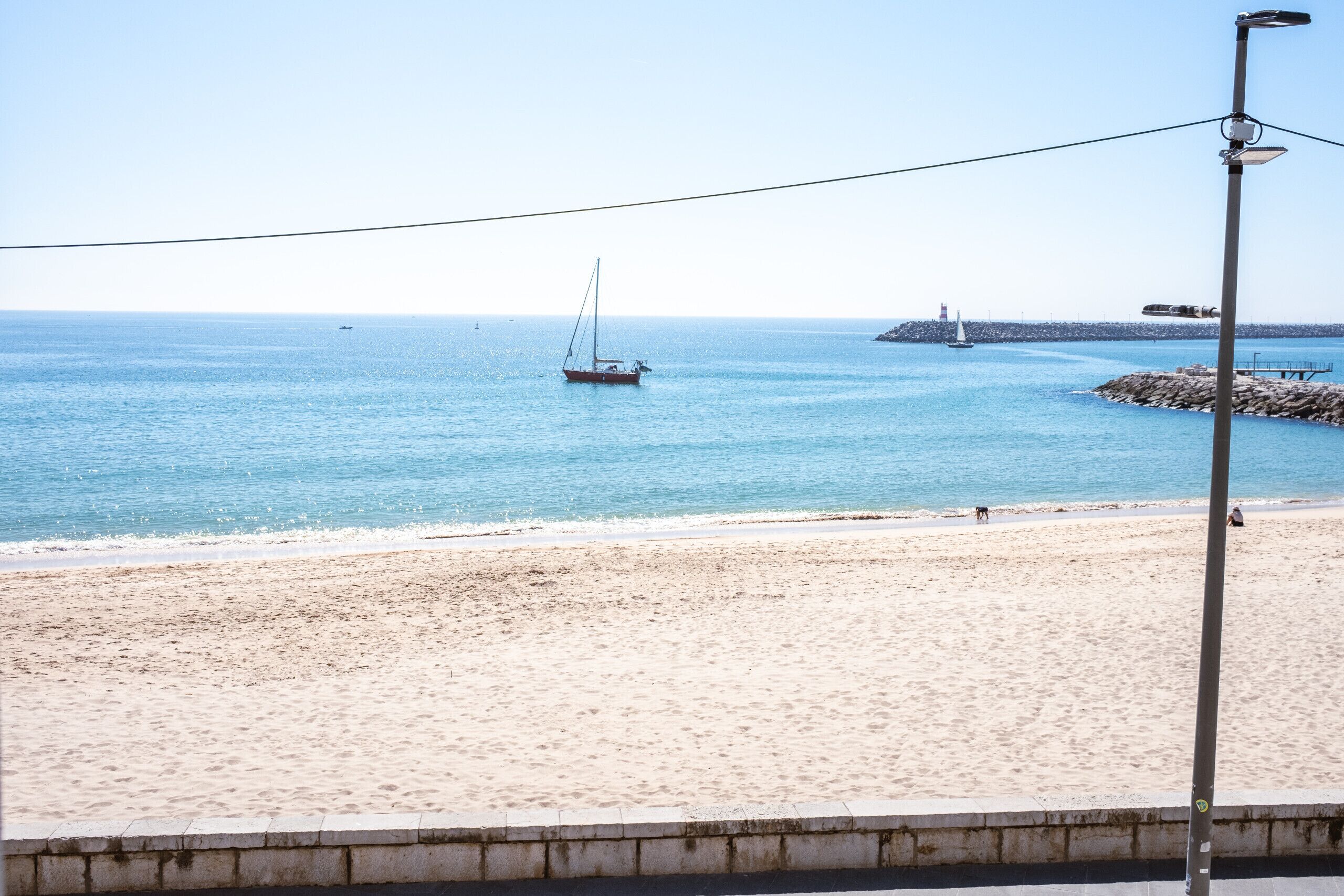 Une plage avec un voilier, un phare et une jetée rocheuse.