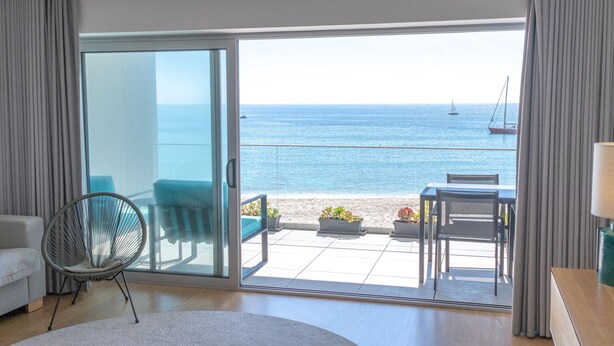 A modern room with a large sliding glass door leading to a balcony with a view of the sea and a sailboat. - Sesimbra Ocean Terrace (Sesimbra)