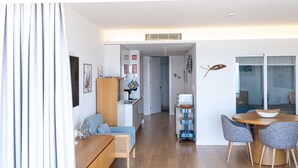 A modern living room with a sofa, a dining table with chairs, a kitchen area, and a sliding glass door leading to another room. - Sesimbra Ocean Terrace (Sesimbra)