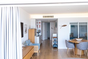 A modern living room with a sofa, a dining table with chairs, a kitchen area, and a sliding glass door leading to another room. - Sesimbra Ocean Terrace (Sesimbra)