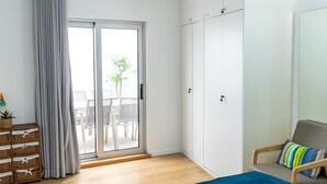 A modern bedroom with a sliding glass door to a balcony, a bed, a chair, and a wardrobe. - Sesimbra Ocean Terrace (Sesimbra)