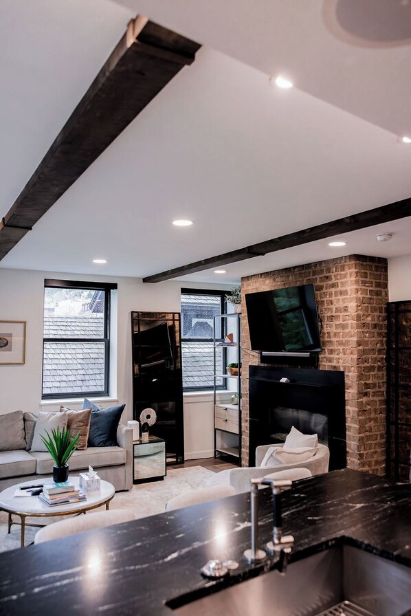 A modern living room with a fireplace, a television mounted on a brick wall, and a sofa. - Park City’s Most Coveted Address on Main - Atticus (Park City)
