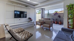 A modern living room with a flat-screen TV, two sofas, a cushioned chair, and potted plants.
