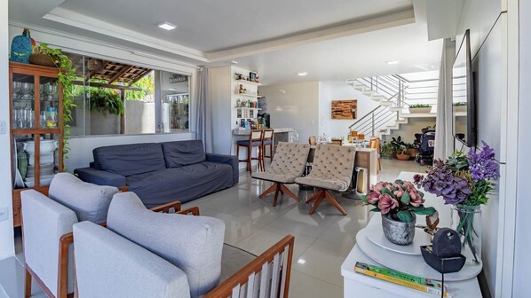 A modern living room with a sofa, armchairs, a dining area, and a staircase.