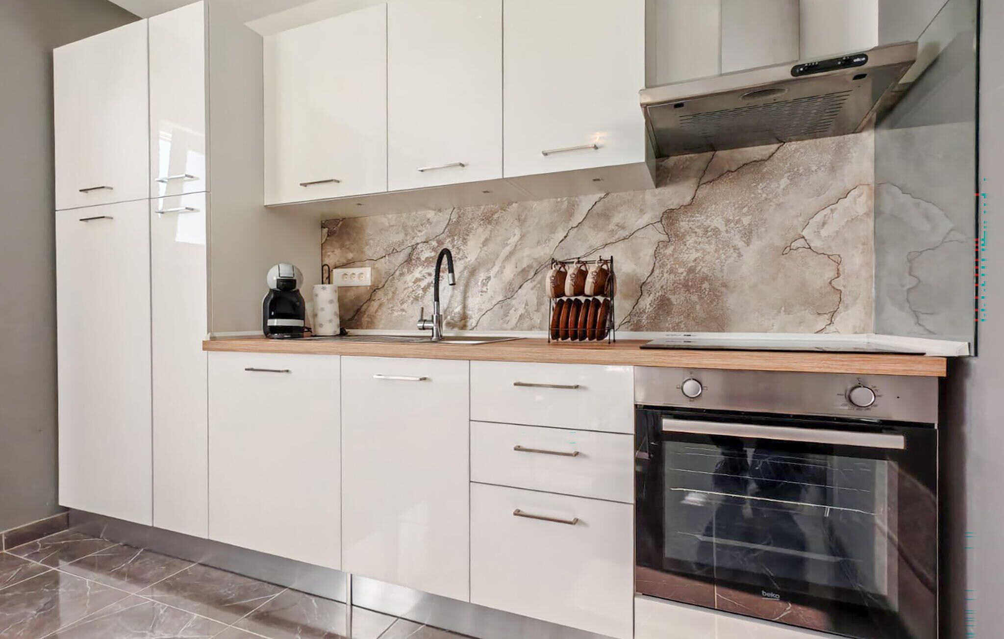 Een moderne keuken met witte kasten, een ingebouwde oven, een koffiezetapparaat en een marmeren achterwand.