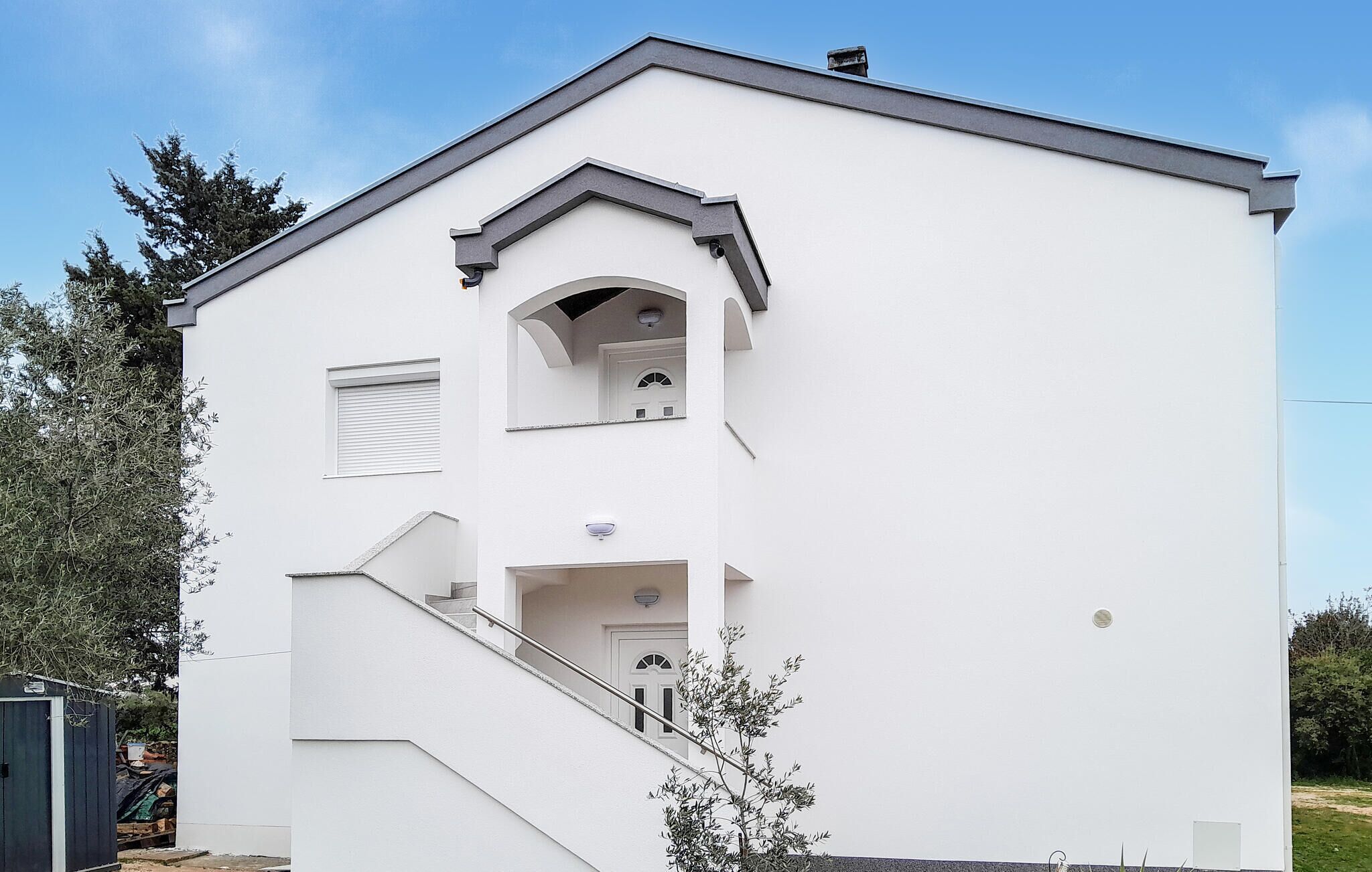 Un bâtiment moderne à deux étages, doté d’une façade blanche, d’un petit balcon et d’un escalier menant à l’entrée.