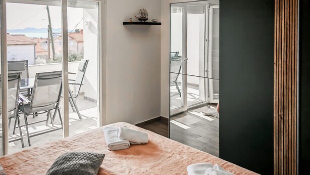 Hotellihuone, jossa on sänky, pieni pöytä, tuoli, parveke, jolta on näkymä, ja ovi.