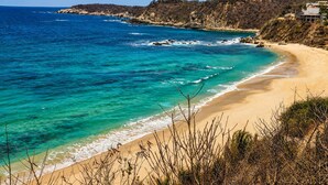 Eine Küstenlandschaft mit Sandstrand, klarem türkisblauem Wasser und steilen Felsen.