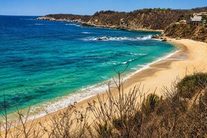 Eine Küstenlandschaft mit Sandstrand, klarem türkisblauem Wasser und steilen Felsen.