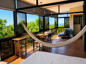 A modern room with large windows, a hammock, a bed, and a dining area. - Penthouse doble, cama Queen, cocina completa y sofa cama (Cuatunalco)