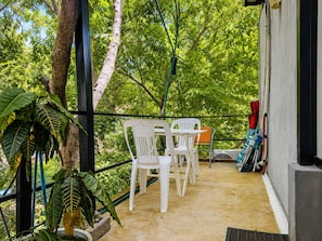 A balcony with white plastic chairs, a small table, and a red chair. There are plants and a white wall with a window. - Penthouse doble, cama Queen, cocina completa y sofa cama (Cuatunalco)