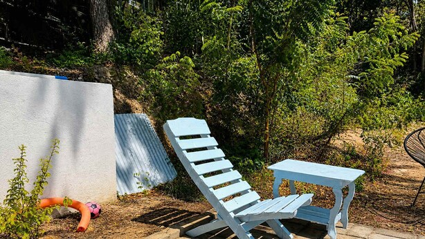 Ein Sitzbereich im Freien mit blauem Stuhl und Tisch, umgeben von Pflanzen und einer weißen Mauer.