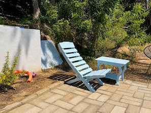 An outdoor seating area with a blue chair and table, surrounded by greenery and a white wall. - Loft, cama Queen, cama individual, cocina completa (Cuatunalco)