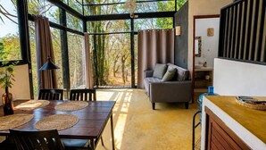 Una habitación amplia con un ventanal grande, un sofá, una mesa de comedor con individuales y una zona de cocina.
