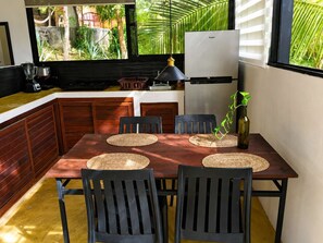 A kitchen with a dining table, chairs, a refrigerator, and a window with a view of greenery. - Loft, cama Queen, cama individual, cocina completa (Cuatunalco)