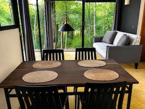 A dining area with a table and chairs, a hanging pendant light, and a sofa with cushions. - Loft, cama Queen, cama individual, cocina completa (Cuatunalco)