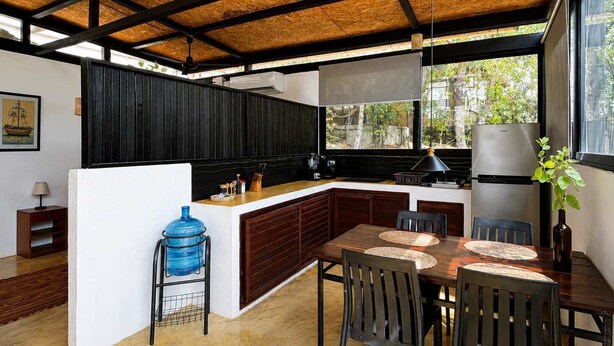 Cocina moderna con techo de madera, comedor con mesa y sillas, y un dispensador de agua grande.