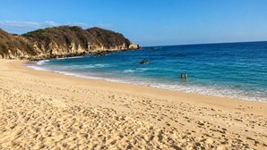 Una playa arenosa con aguas azules cristalinas y acantilados rocosos al fondo.