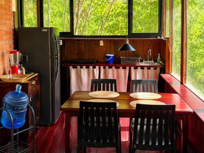 A compact kitchen with a dining area, a water dispenser, and a view of greenery through the windows.