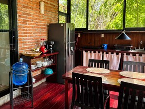 A kitchen with a brick wall, a refrigerator, a sink, and a dining table with chairs. - Bungalow doble, cama Queen, cama individual y terraza exterior cocina completa y sofa cama (Cuatunalco)