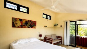 Un dormitorio con cama, una silla, ventilador de techo, ventana y estante de pared.